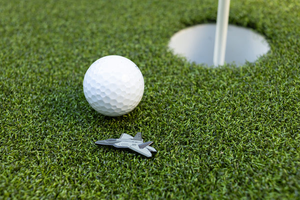 "F-22 Raptor" ball marker by Tall Pines Golf, next to a golf ball on the green